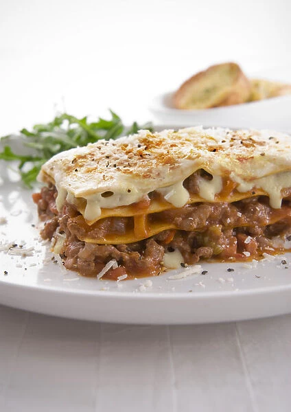 Traditional lasagne made with beef, pancetta and vegetables, served with rocket and bread, close-up