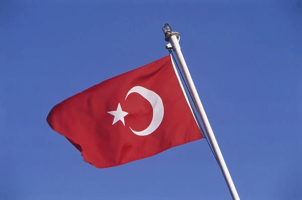 Turkish flag on white flagpole blowing in the breeze, deep blue sky in background
