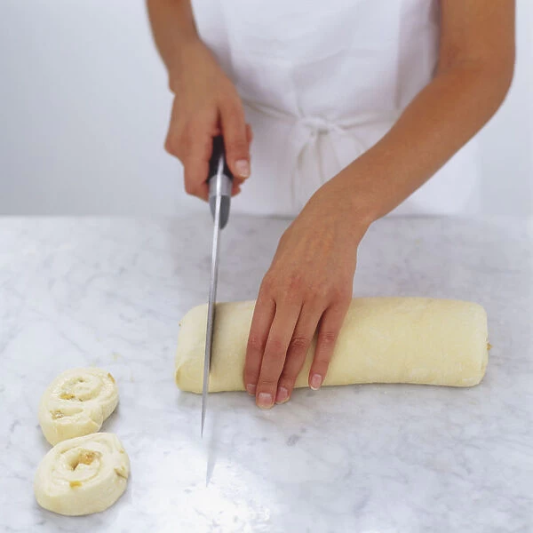 Uncooked pains aux raisins roll being sliced, high angle view