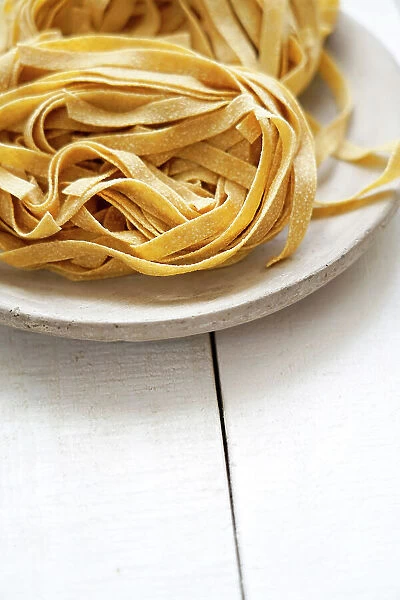 Uncooked whole wheat tagliatelle on a white wooden background, Italy, Europe