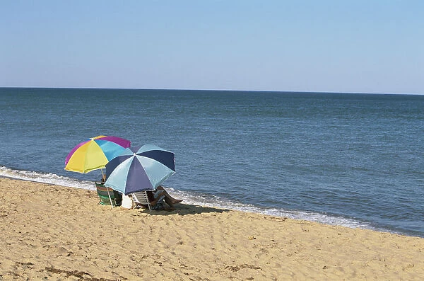 USA, Rhode Island, Misquamicut State Beach, rear view of two people sitting under parasols looking out to sea