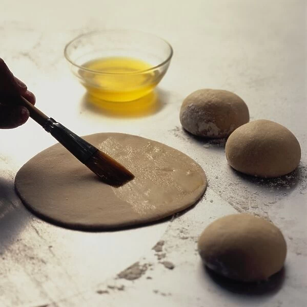 Using basting brush to coat ghee on circle of flat tawa paratha bread dough, close-up