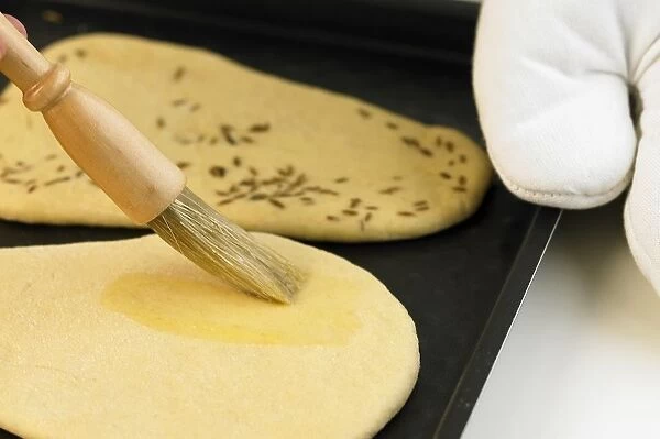 Using basting brush to glaze naan bread on baking tray