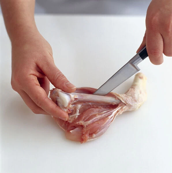 Using kitchen knife to cut around bone of chicken drumstick and freeing it from flesh