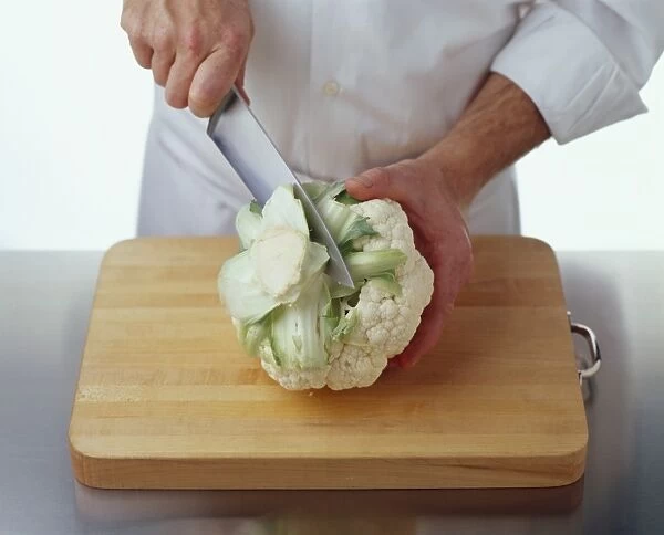 Using kitchen knife to cut stem base from cauliflower on chopping board