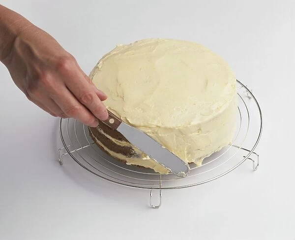 Using kitchen knife to spread buttercream on top and side of layered sponge cake on rack