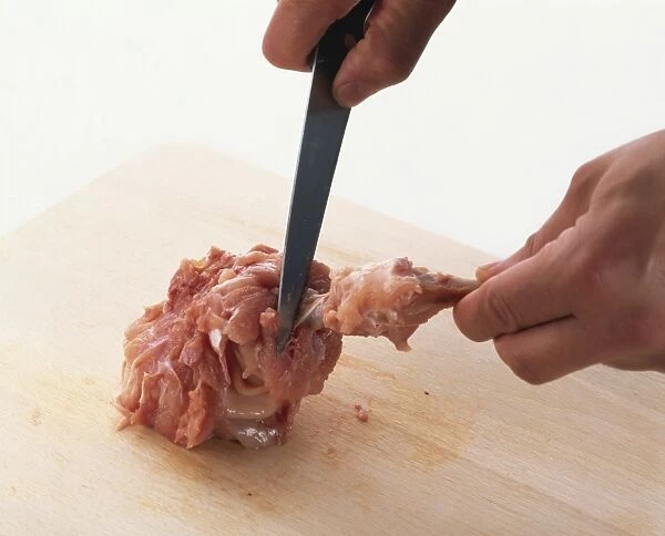 Using small kitchen knife to bone chicken lead on wooden chopping board, close-up