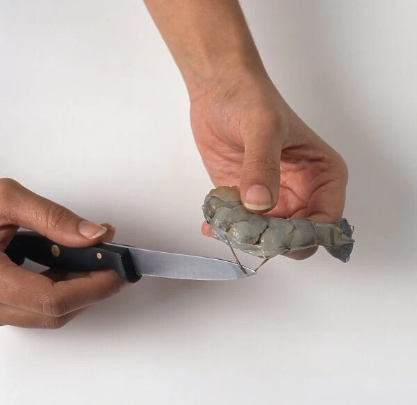 Using small kitchen knife to remove intestines from raw prawn