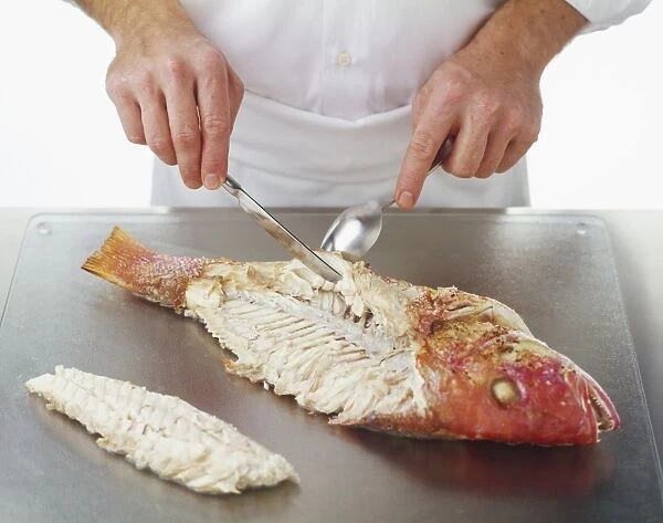 Using a spoon and a knife to remove fillets from a cooked Red Snapper