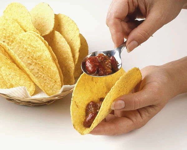 Using a spoon to fill a taco shell, close up