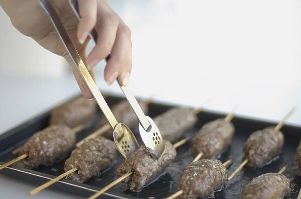 Using tongs to turn lamb kebabs on baking tray