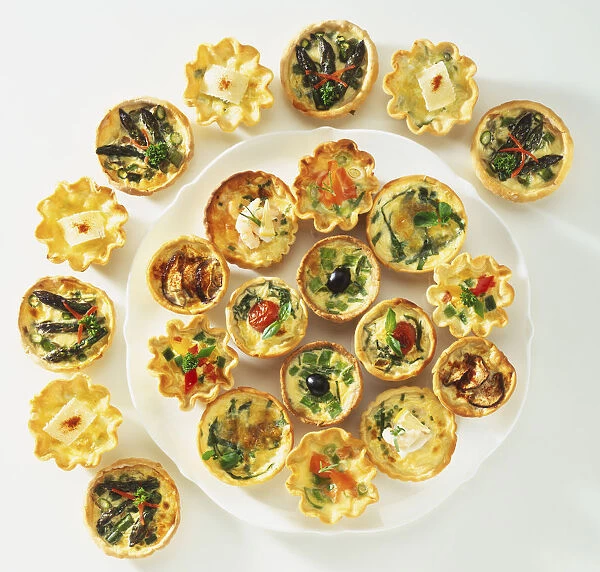 Various small quiches on a platter and in a semi-circle around it, view from above