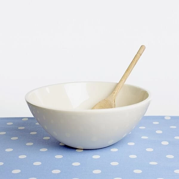 Empty white bowl with wooden spoon on blue and white polka dot tablecloth, close-up