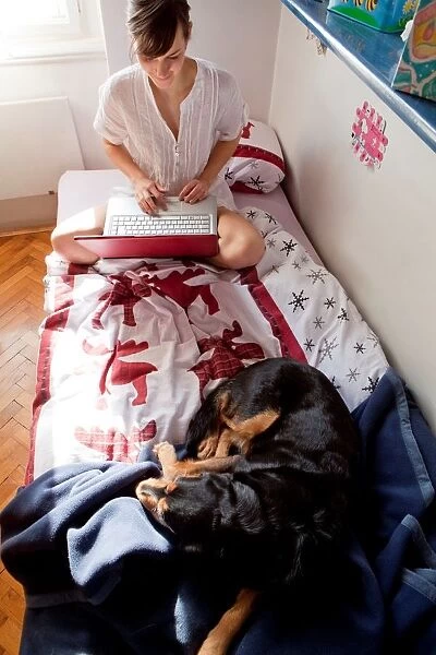 A Woman Sitting on the Bed to Computers with a Dog