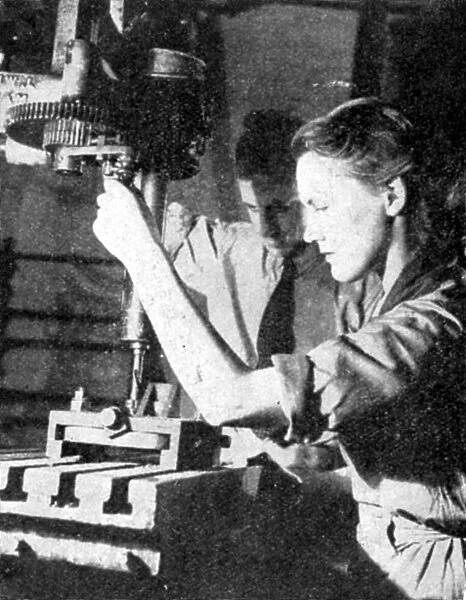 Woman in tank factory being instructed in the use of a metal power drill: 1940. World War II