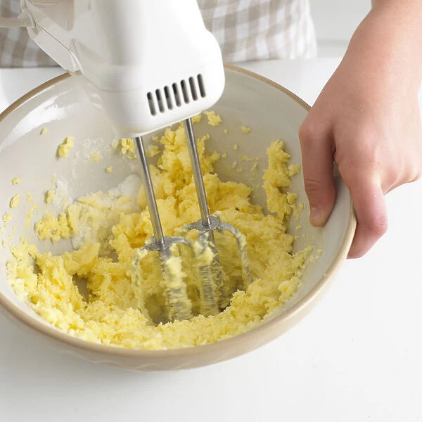 Woman using electric mixer to beat sugar and butter in bowl