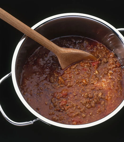 Wooden spoon stirring bolognese sauce in saucepan, view from above