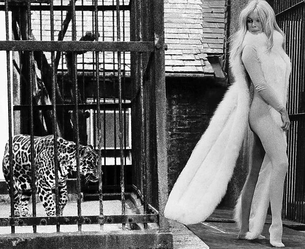 Brigitte Bardot French actress in skin tight catsuit with fur cape standing beside cage