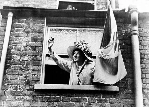 A Suffragette leaning out of a window, waving and holding a banner. Circa 1912