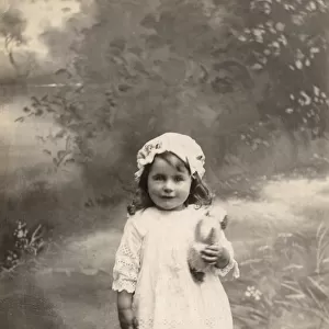 A little girl in lacy dress and cap poses with a toy bulldog Date: circa 1915