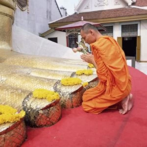 Buddhist monk kneeling and praying at the feet of a standing Buddha