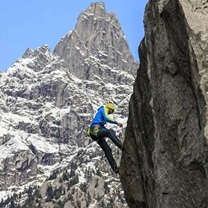 Climber on steep rock face in the background blue sky and peaks of the Alps, Masino Valley