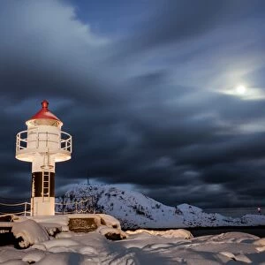 Lighthouse and full moon in the Arctic night with the village of Reine in the background