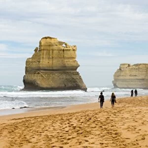 People walk along a beach with one of the Twelve Apostles geological formation in the background