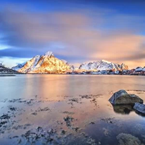 The pink sky at sunrise illuminates Reine village with its cold sea and snowy peaks