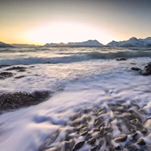 The sunset light reflected on the waves of cold sea crashing on the rocks, Djupvik