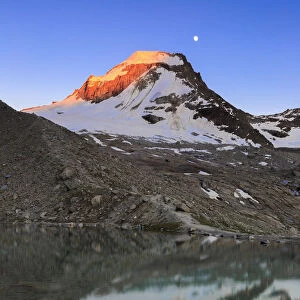 Ciarforon still illuminated by the colors of dawn and the moon are reflected in Moncorv√® lake. Valsavarance, Gran Paradiso National Park, Aosta Valley, Italy