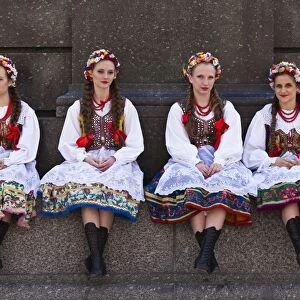 Poland, Cracow. Polish girls in traditional dress sitting at the base of the statue of Adam Mickiewicz, preparing to dance in