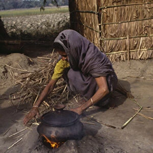 BANGLADESH Woman cooking on small open fire with cooking pot held on raised clay