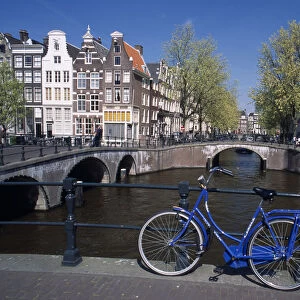 HOLLAND, Noord Holland, Amsterdam Blue bicycle leaning against a railing on bridge