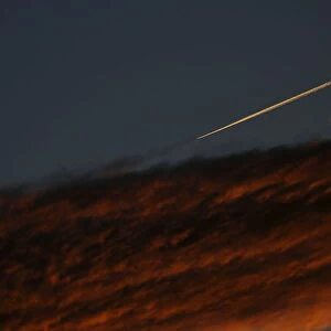An airplane leaves a vapor trail as it flies past a cloud during dusk as seen