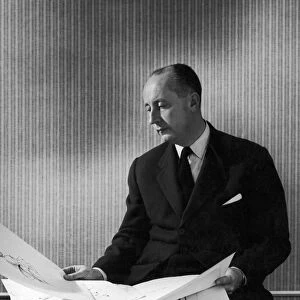 CHRISTIAN DIOR (1905-1957). French fashion designer. Dior looking over some of his sketches for womens dresses, 1940s or 1950s
