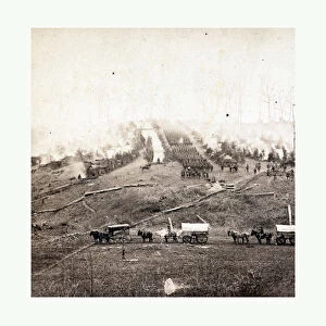 American Civil War: Three Horse-drawn Covered Wagons In The Foreground. Soldiers Marching In Formation Between Rows Of Small Cabins And Tents In The Background. Photo