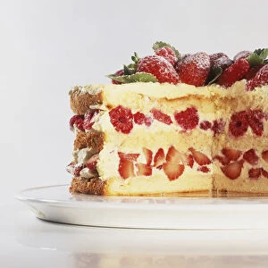 Biscuit de Savoie, layered cake with slice removed, strawberries and raspberries nestling with cream between cake layers, fresh fruit and leaves decorating top