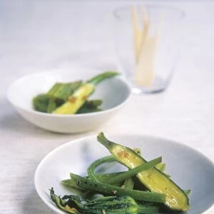 Bowls of stir-fried greens with garlic and a glass containing small wooden forks in the background