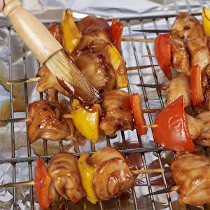 Brushing barbecue sauce onto chicken and pepper kebabs with pastry brush