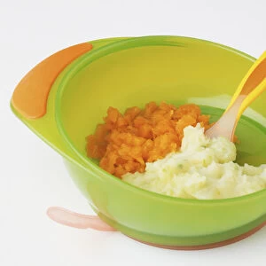 Carrot and potato puree served in green plastic bowl with yellow plastic spoon embedded