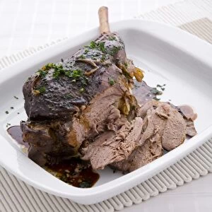 Carved, roasted lamb in gravy, garnished with parsley, on serving dish, close-up