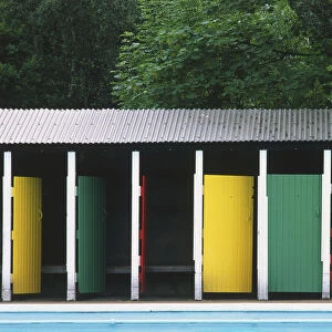 Changing rooms with brightly painted doors and corrugated iron rook, standing by an outdoor swimming pool
