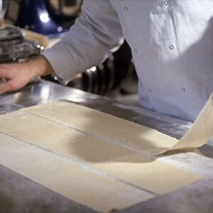 Chef placing sheet of fresh pasta on worktop, pasta machine nearby