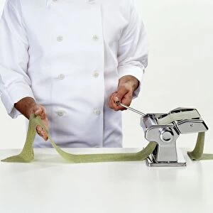 Chef rolling spinach pasta dough through a pasta machine