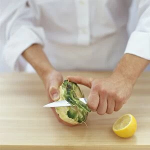 Chef using kitchen knife to remove base from globe artichoke on wooden chopping board