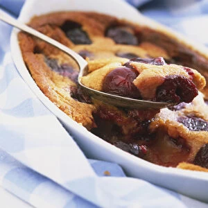 Cherry clafoutis being spooned out of oval white dish, close up