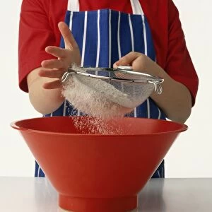 Child sifting flour into red mixing bowl