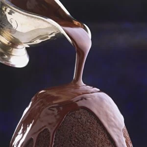 Chocolate sauce being poured over small chocolate cake, close up