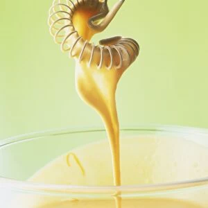 Close-up of orange juice added to a Maltaise sauce dripping from a flat-coiled wire whisk into a glass bowl